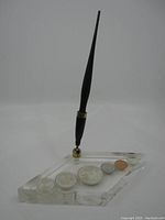 Clear angled acrylic base embedded with six coins and black fountain pen held upright.