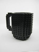 Front and side view of black Lego block style coffee mug showing studded texture and angular handle.