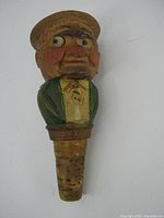 Front view of a vintage hand carved wooden mechanical cork stopper depicting a man's face with googly eyes and painted details, attached to cork stopper portion.