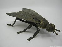 Side angled view of brass fly ashtray showing detailed wings, body, and legs with antique patina.