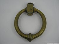 Front view of Victorian solid brass door knocker showing circular ring and mounting bracket with aged brass finish and some surface wear.