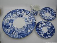 Four blue and white Royal Crown Derby Mikado dishes including small creamer, large plate, and two saucers, all in used condition with wear visible