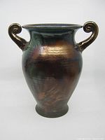 Front view of signed raku vase showing rounded body and curled handles with iridescent glaze.