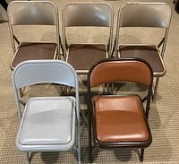 Set of five folding chairs, three beige with vinyl backs and seats, two padded chairs in gray and brown.