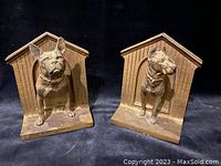 Full view of both bookends showing two different dogs standing in front of dog house backdrops, brass-washed cast iron with some dust and scratches.