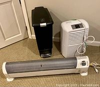 Three items shown together: black SimpleHuman trash can with step lid, white LG dehumidifier, long Honeywell floor heater on carpet