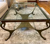 Full view of rectangular bronze-finished metal coffee table with beveled glass top placed on carpet with cream sofa in background.
