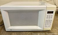 Front view of the white GE microwave oven showing the door with glass window and keypad panel on the right side.