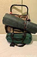 Side angled view of the Coleman Exponent backpack loaded with green sleeping bag and inflatable pad on top, showing straps and carry handles.