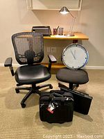 Office chairs, portfolio, business case, and clock arranged near a small desk with a halogen lamp on top.