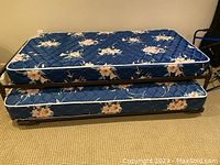 Side view of two stacked floral patterned mattresses in blue with pink flowers, showing thickness and cover detail.