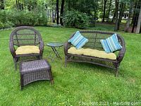 Three-piece resin wicker patio furniture set with armchair, two-seat love seat, rectangular ottoman, and small round side table with cushions, shown outdoors on lawn.