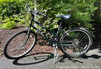 Full side view of green Ross Mt. Pocono women's mountain bike outdoors with shadows and greenery background. Shows overall frame, wheels, seat, pedals, chain, and handlebar.