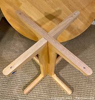 View of bottom of table showing screw-in connection points of pedestal base to tabletop, four supporting legs extending outward from pedestal post.