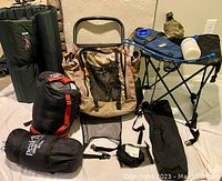 Complete set of hiking and camping gear on white background showing backpack, rolled tent and sleeping bags, hydration packs, and pop-up seat/table