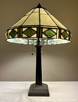 Full view of the lamp powered on showing the illuminated leaded glass shade and dark metal base.