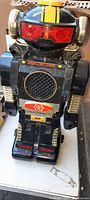 Front view of the 12 inch black vintage robot toy. Shows red eyes, speaker grill, yellow stripe on the head, and metallic details on arms and sides of head.