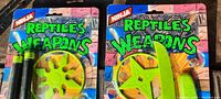 Front packaging view of two unopened 1980s Ninja Reptiles Weapons toy accessory packs showing colorful comic-style graphics and bright yellow weapon props.