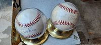 Two vintage autographed baseballs inside clear plastic collector display domes with brass-colored bases, signatures visible on balls.