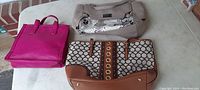Three ladies designer handbags displayed on a surface: pink pebbled tote, taupe and snake print satchel with maker tag, beige and brown patterned handbag with gold-tone details.