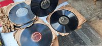 Photo of 78 RPM shellac records stacked on crumpled paper, showing black records with different label colors including red and black.