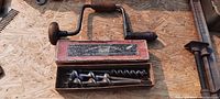 Photo showing the hand held boring drill with wooden handle and its original wooden box with label visible containing some drill bits.