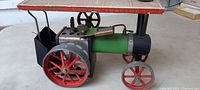 Side view of antique steel steam engine toy tractor showing red wheels, green boiler, black smokestack and white roof with red lettering