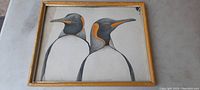 Framed print showing two king penguins, with detailed illustration and wooden frame.