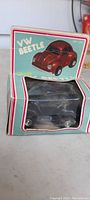 Photo shows the original box with teal background and clear plastic window containing a red VW Beetle friction toy car, box labeled 'VW beetle' and 'friction'.