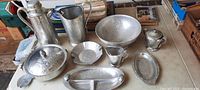 Full collection of hammered aluminum antique serving tableware displayed on table including lidded casserole, coffee percolator, pitchers, divided serving tray, bowls, sugar bowl, creamer, and plates.