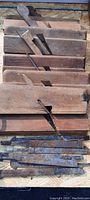 Grouping of multiple antique wooden hand planes with metal blades intact, arranged in stacks, visible aged wood and metal blades.