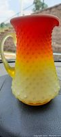 Front angled photo of the multicolor hobnail glass pitcher showing color gradient and handle.