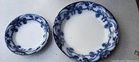 Top view of two round antique dishes with blue floral decoration and gold tint accents, showing size difference.