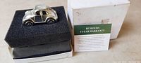 Small pewter Volkswagen Beetle-shaped clock inside black foam insert with original white box and warranty paperwork.