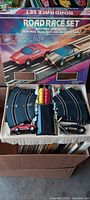 Open box showing road race slot cars on curved track pieces arranged inside with magnetic base in center.
