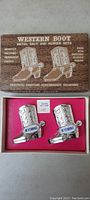 Original box with wood-grain lid, showing printed title and description of the Western Boot Salt and Pepper Sets, and inside the box are two metal boot-shaped shakers with Wyoming labels.