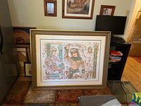 Framed lithograph leaning against wall on floor
