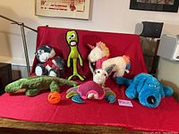 Photo showing seven large dog toys on a red blanket, including plush animals and rubber toys.