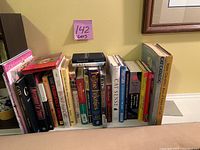 Photo shows a row of various cat books arranged upright on a shelf, showing titles related to cats including care, stories, and pictures.