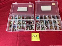 Two clear plastic organizers with hinged lids open, showing compartments filled with assorted earrings organized by pairs.
