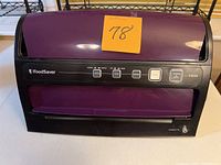 Closed FoodSaver vacuum sealer in black and purple color with control buttons on front panel and sticky note with number 78 on top.