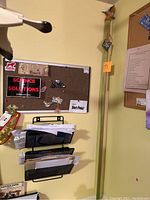 Photo showing the full length of the wooden hiking stick leaning against a wall near a bulletin board and documents.