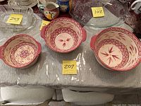 Set of three nesting round bowls with handles, arranged side by side to show different sizes and decorative patterns in red on beige.