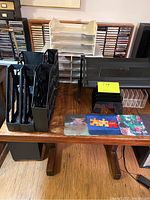 Photo showing multiple office organizers and accessories on a wooden table, including magazine holders, paper sorter, in/out trays, letter sorters, and mouse pads.