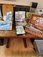 Wide view of the boxed and basketed sewing supplies including bobbins, hoops, fabric, patterns, and books.
