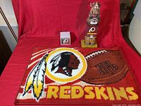 Full view of the three Washington Redskins collectibles on red backdrop featuring rug, totem pole, and paper cube.