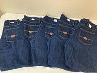 Five pairs of unfolded dark blue denim jeans laid flat, showing back pockets and Red Kap branding patch.