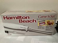 Box showing Hamilton Beach Carve 'n Set electric knife with case, features include compact storage case, non-slip trigger, easily carves meats and slices breads, stainless steel blade and carving fork