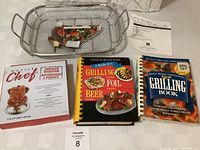 Photo showing mesh grilling pan with food example, chicken roaster box, two grilling cookbooks, and printed information sheet.
