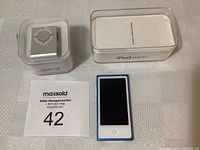 Blue Apple iPod Nano next to its clear plastic case and original packaging with 16GB label visible.